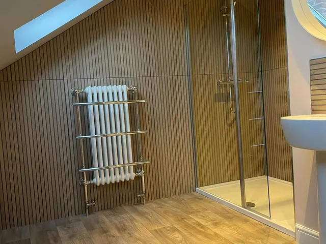 Loft bathroom with a walk-in shower, wood slat wall panelling, a chrome and white column towel radiator, pedestal basin and roof windows in the sloping ceiling