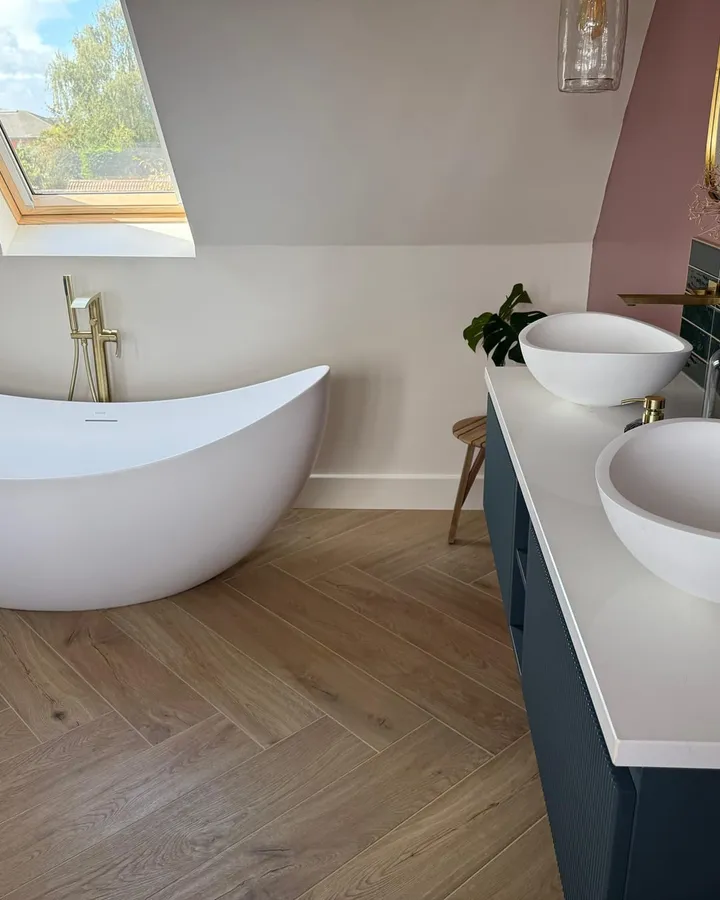 Loft bathroom with a freestanding slipper bath beneath a roof window, beside a double vanity with two basins
