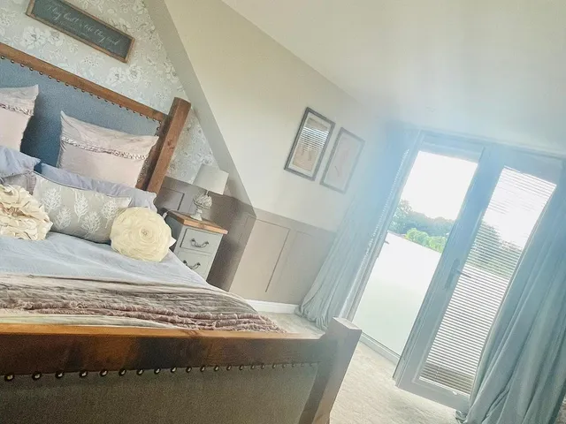 Sunlit loft bedroom with a dark wooden bed, floral feature wall and French doors with long curtains