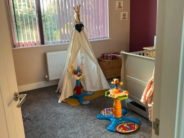 Children's room in a loft conversion with grey carpet, a play teepee, a cot and a deep red feature wall