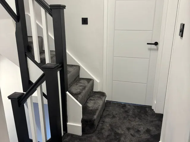 Landing with charcoal carpeted stairs, black-painted newel posts and handrail, white spindles and a white panelled door