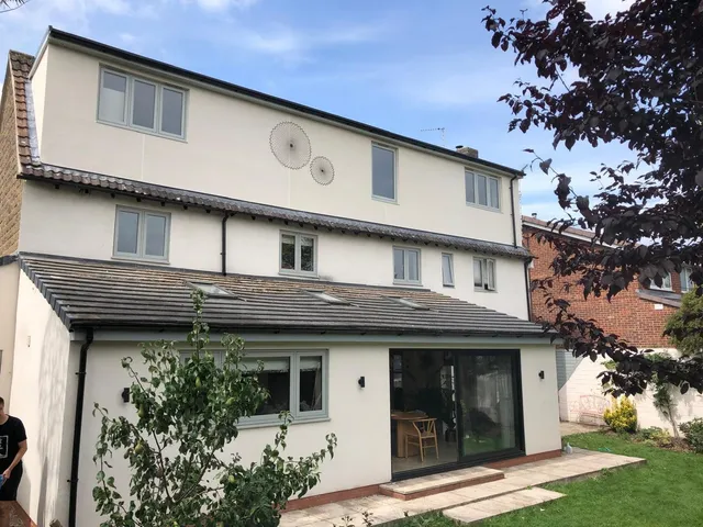Rear of a white-rendered three-storey house with a full-width rear dormer and an extension opening onto the lawn