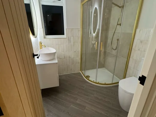 Loft shower room with a brass-framed quadrant shower, oak door, white vessel basin and wood-effect floor