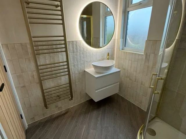 Shower room with a floating white vanity and round mirror between a brass towel radiator and a brass-framed shower