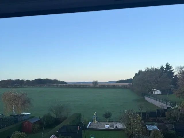 View from a new loft window over back gardens to open fields under a clear sky
