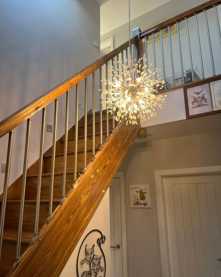Timber staircase with metal spindles and a starburst chandelier leading up to a loft
