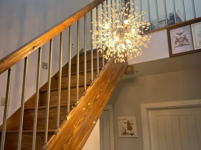 Timber staircase with metal spindles and a starburst chandelier leading up to a loft