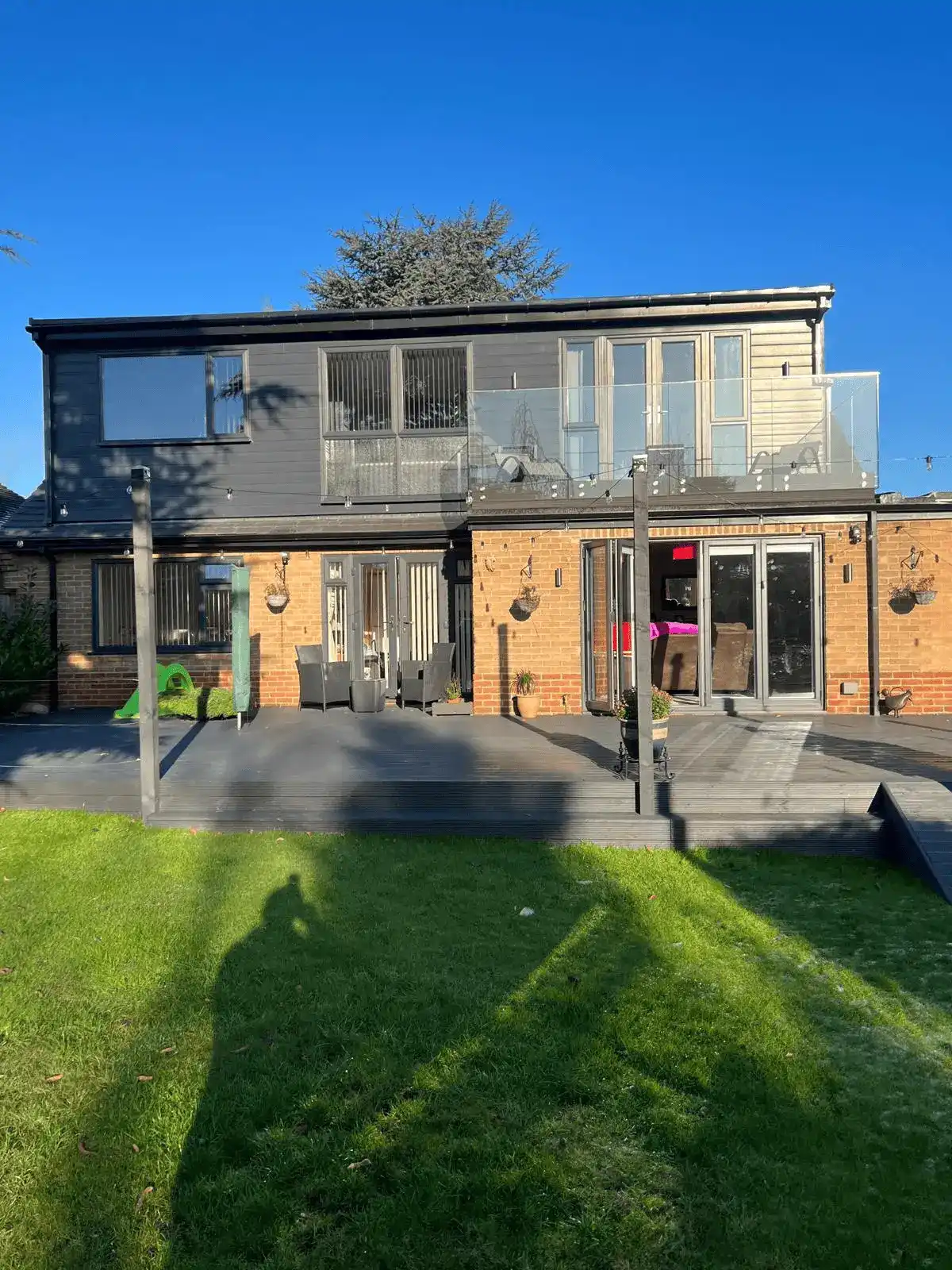 Rear dormer loft conversion with glass balconies overlooking a sunny back garden