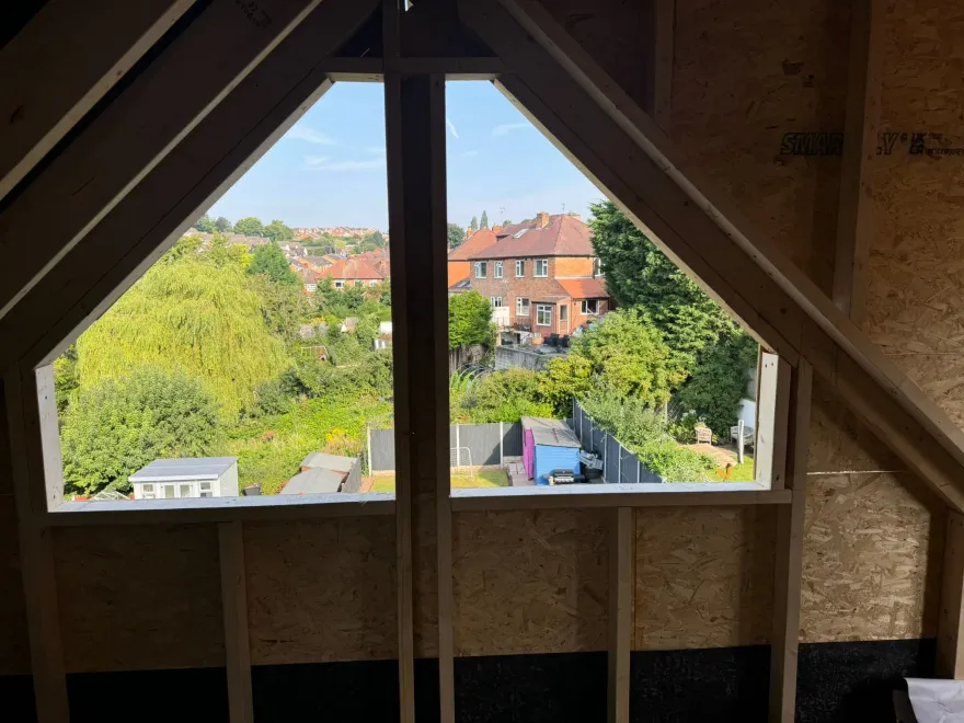 Timber-framed gable window opening in a loft conversion, looking out over rooftops and trees